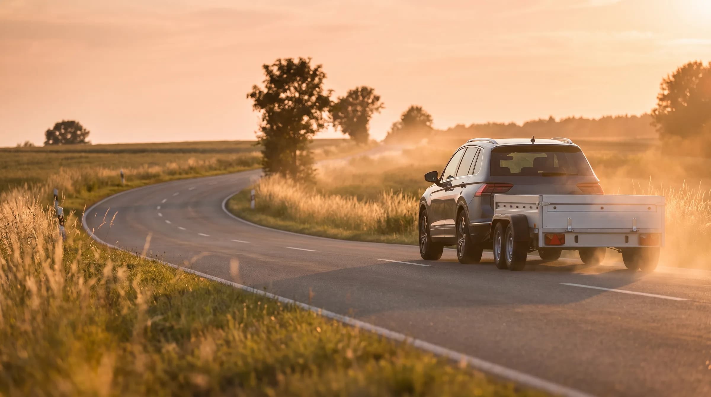 Véhicule tractant une remorque plateau sur une route de campagne au coucher du soleil