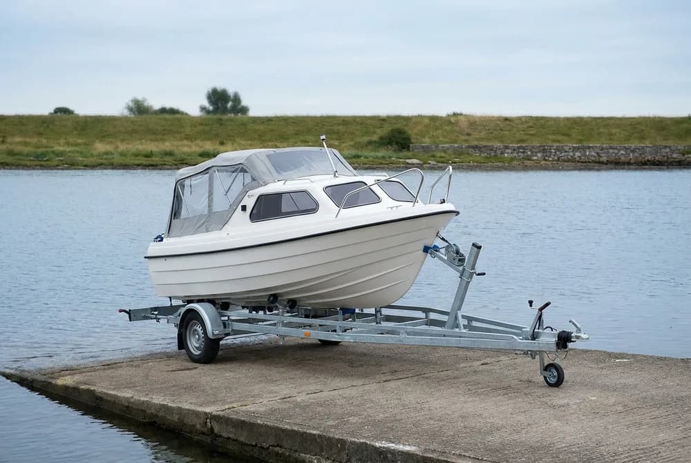 Porte-bateau galvanisé supportant un petit bateau à moteur blanc, sur une cale de mise à l'eau