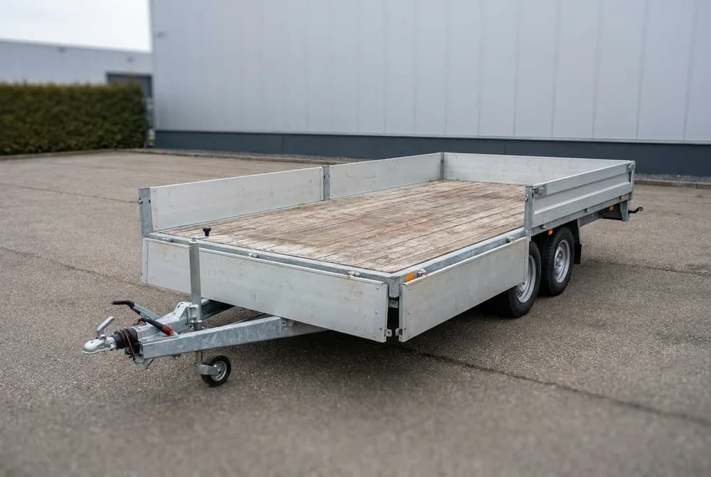 Remorque plateau à ridelles basses, plancher bois vide, stationnée sur une cour pavée